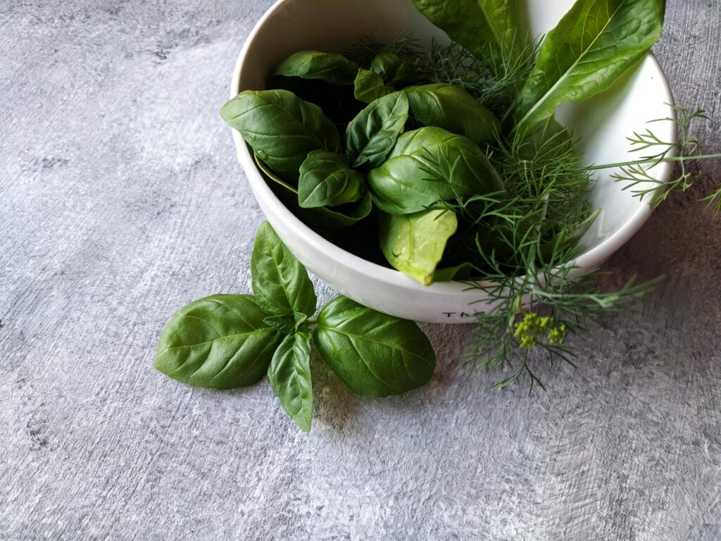 Close-up of fresh basil and herbs in a bowl on a gray background.