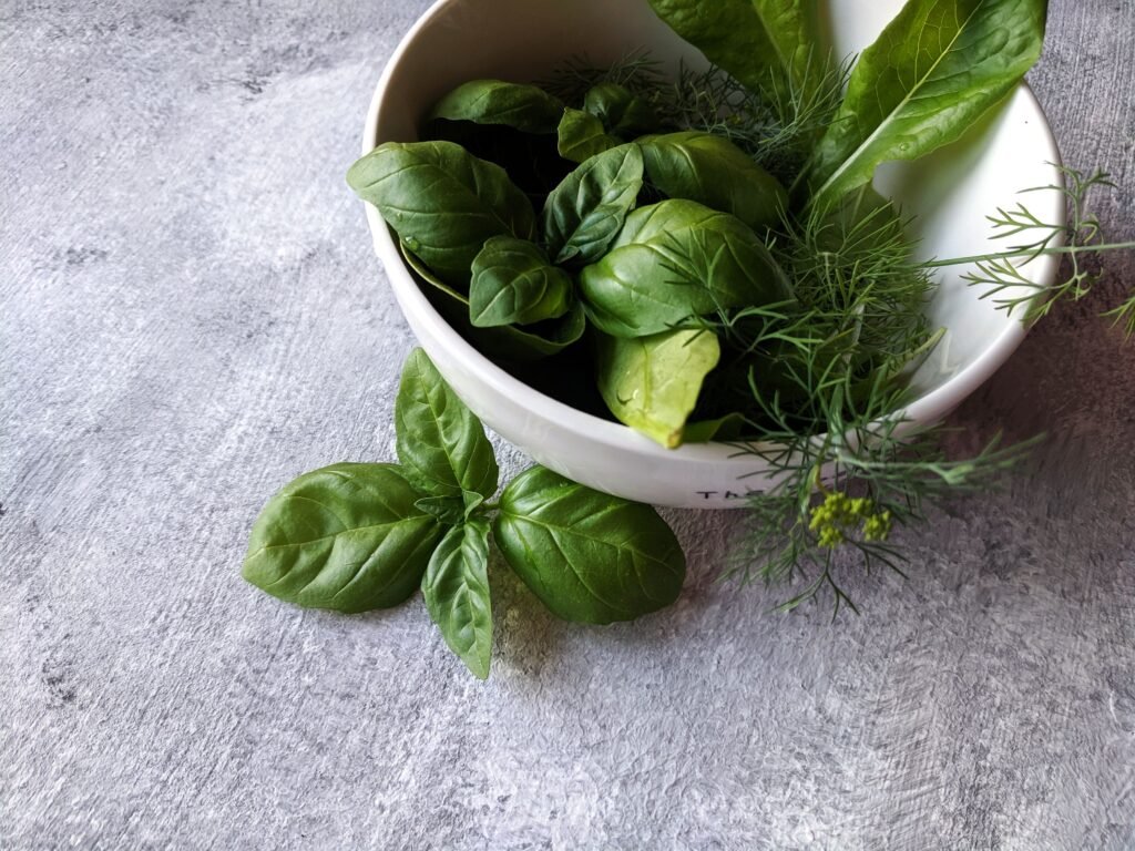 Close-up of fresh basil and herbs in a bowl on a gray background.