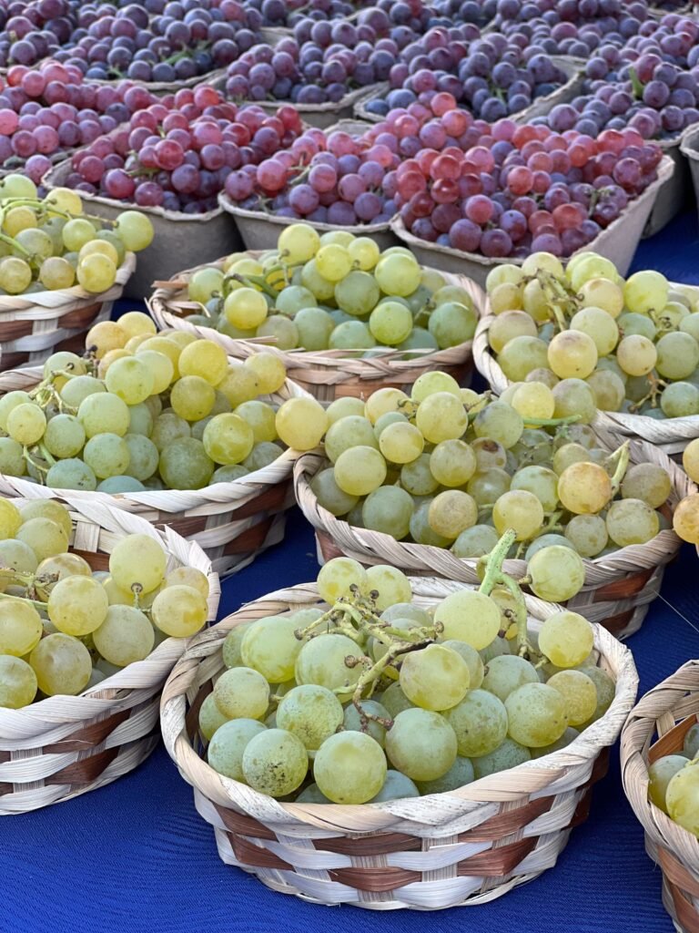 Close-up of white and red grapes at a market stall in wicker baskets.