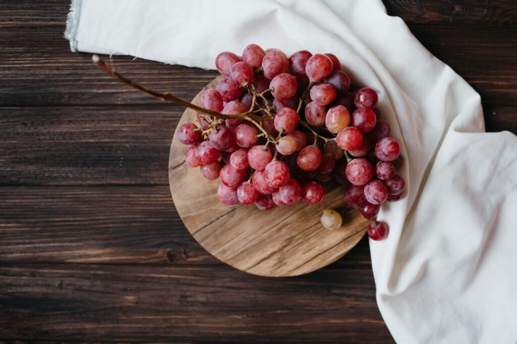 High angle shot of fresh ripe grapes on a wooden board with a white cloth background.