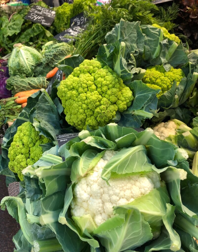 Vibrant display of fresh cauliflower and broccoli at an outdoor market.